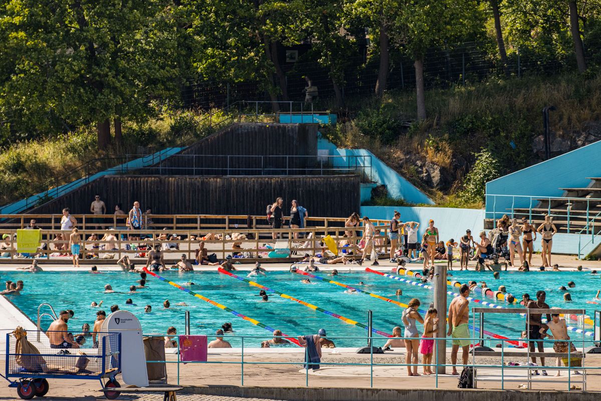 Volles Freibad an einem Sommertag, Menschen im Becken und auf den Rängen.