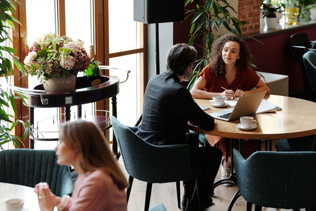 Gespräch an einem runden Tisch mit Laptops und Kaffee.