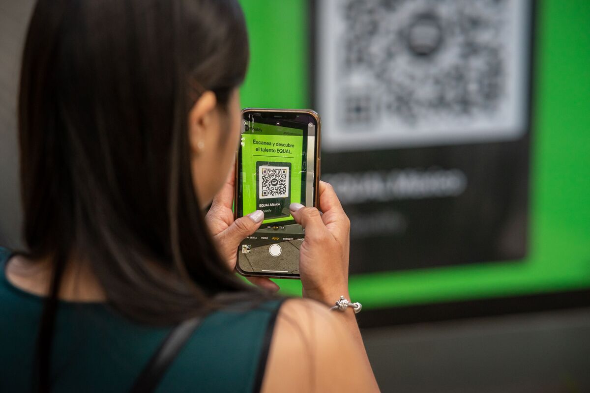 Eine Frau scannt mit dem Smartphone einen QR-Code an einem Bildschirm.